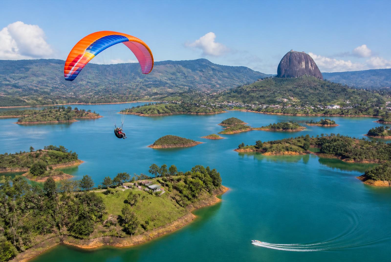 Parapente sobre el embalse verde de Guatapé con un jetski dejando estela en el agua